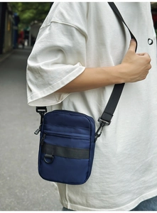 Outdoor shot of a compact navy blue men's messenger bag with multiple zipper compartments