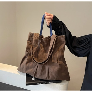 Detail of dark brown canvas tote bag featuring denim handles and stylish bottom pleat design