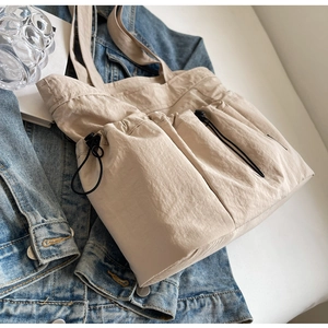 Detailed view of beige pleated tote bag featuring functional external drawstring pockets