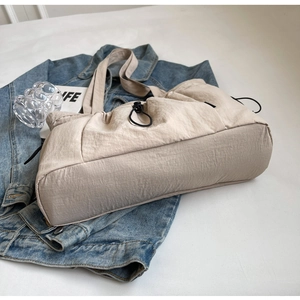 Detail of beige pleated nylon tote bag featuring adjustable black drawstring closure
