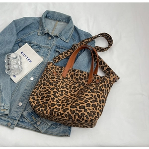 Leopard print canvas tote bag featuring brown leather handles and adjustable shoulder strap