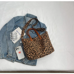 Detail of leopard print canvas tote bag with leather handles and blue denim jacket