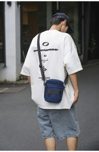 Detail of a dark blue nylon crossbody bag with adjustable strap and functional zipper pockets
