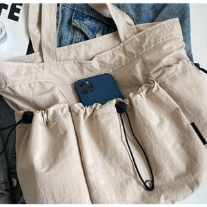 Detail view of the beige pleated tote bag showing a side pocket holding a smartphone