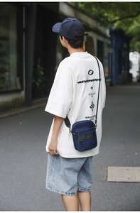Outdoor street view of a man wearing a blue nylon crossbody bag with casual summer outfit