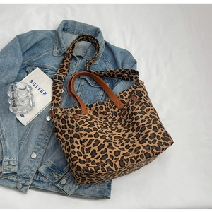 Close-up of leopard print canvas tote bag with brown leather handles on denim jacket