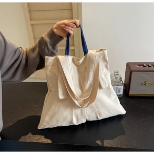 Detail view of cream canvas tote bag with contrast blue handles and orange stitching