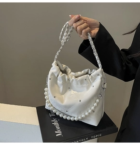 Detail of white glossy bucket bag with quilted stitching, metal studs, and pearl handle