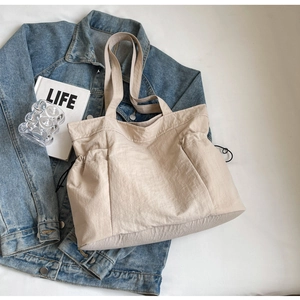 Close-up of beige pleated nylon tote bag with wide shoulder straps on a denim jacket