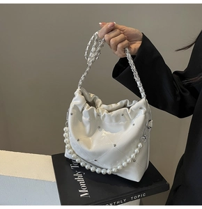 Detail of white quilted cloud bucket bag with pearl strap and silver rivet accents