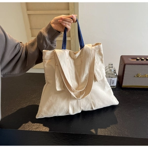 Detail of cream canvas tote bag with blue straps showing handles and shoulder strap