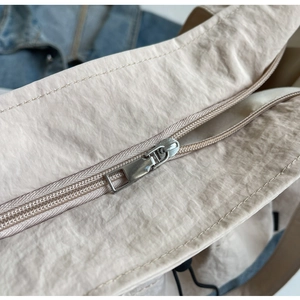 Detail of silver metal zipper and pleated nylon texture on beige shoulder tote bag