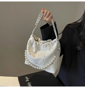 Detailed macro of white glossy bucket bag with pearl chain and silver stud accents