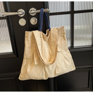 Detail of canvas shoulder bag with vertical stitching and blue denim handles