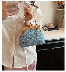 Detail of blue denim shell bag with wooden frame closure and white pearl handle strap
