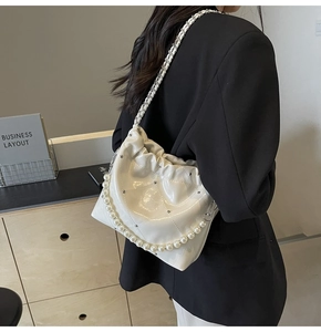 Model wearing a cream ruched cloud shoulder bag with elegant pearl and chain straps