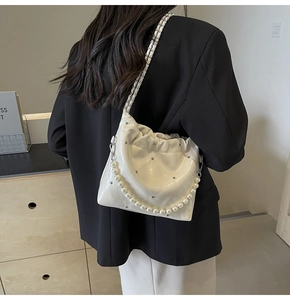 Detail of white quilted patent leather bag with pearls and silver studs shown on model
