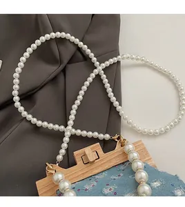 Detail of beaded white pearl strap with gold lobster clasps on blue denim sequin bag