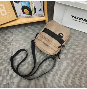 Detail view of khaki nylon messenger bag with adjustable strap on a grey textured mat