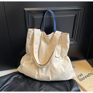 Detail of canvas tote bag featuring orange contrast stitching and blue denim handles