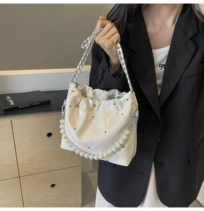 Detail of white quilted bucket bag with pearl handle, chain strap, and metallic studs