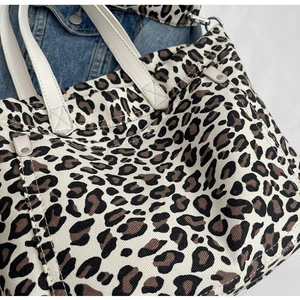 Detailed close-up of leopard print canvas tote bag texture with white handles and silver hardware