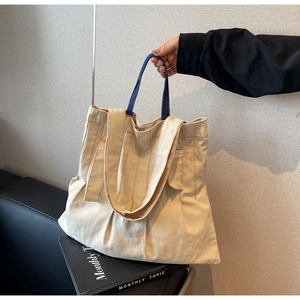 Detail of cream canvas tote bag with contrast brown stitching and blue denim handles