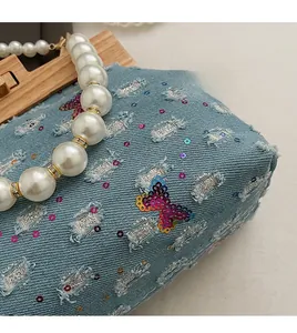 Detail of blue denim shell bag with butterfly sequins and chunky white pearl handle
