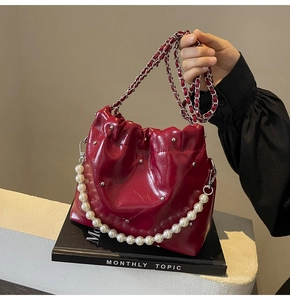 Close-up of deep red quilted bucket bag with pearl handle and silver metal rivet details