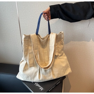 Detail of cream canvas tote bag featuring contrast stitching and dual denim handles