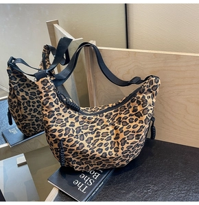Detail view of leopard print crescent bag with adjustable wide strap and woven zipper pull