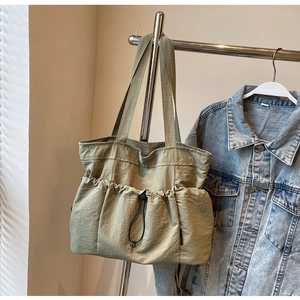 Close-up detail of light green tote bag featuring a pleated drawstring pocket and wide straps