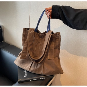 Detail of a brown canvas tote bag with contrast blue handles and vertical stitching on it