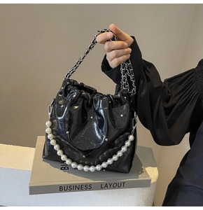 Close-up of black glossy pleated bucket bag with pearl handle and metal chain detail