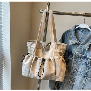 Detail of a large off-white pleated tote bag with multiple drawstring side pockets
