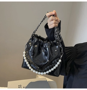 Detail of glossy black pleated bucket bag featuring pearl handle and silver chain strap