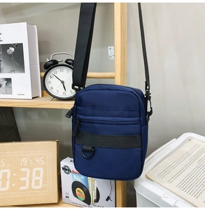 Navy blue crossbody bag with multiple zip pockets hanging in a modern lifestyle setting