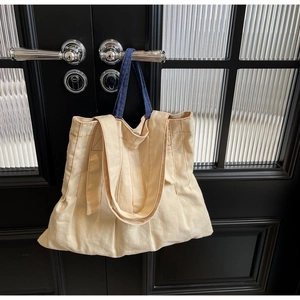 Close-up of canvas tote bag with orange stitching and blue denim handle on door handle
