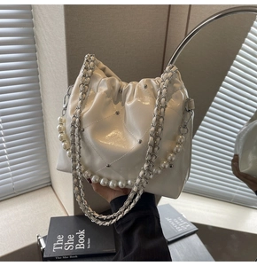 Detail of white quilted bucket bag featuring silver studs and elegant pearl chain handle