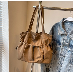 Close-up of brown pleated tote bag with drawstring pocket hanging with a denim jacket