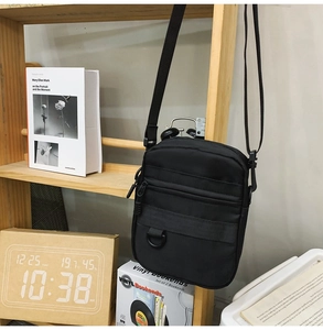 Detailed view of black nylon crossbody bag with zipper pocket and D-ring on wood shelf