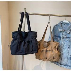 Detail of black and khaki pleated tote bags with drawstring pockets on a metal hanger