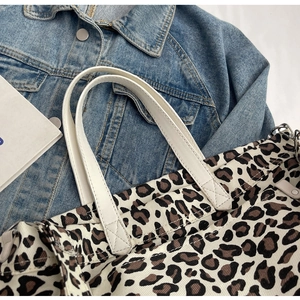 Close-up of leopard print canvas tote bag with white leather handles and metal hardware