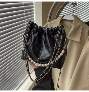 Detail of black quilted bucket bag featuring a pearl chain and metallic studs