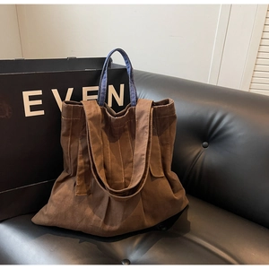 Detail view of brown canvas tote bag with denim texture handle and pleated design on sofa