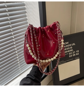 Detail of burgundy bucket bag with glossy leather, silver rivets and pearl chain strap
