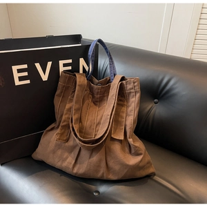 Detail of a brown canvas tote bag with contrast denim handles and stitching on a sofa