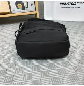 Detailed side view showing the thick base and D-ring of a black nylon crossbody bag