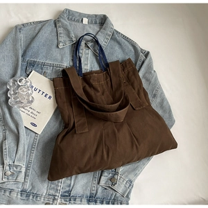 Deep brown canvas tote bag detail with wide strap and blue webbing handle on denim jacket