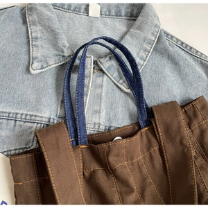 Detail of vintage brown canvas bag featuring blue denim handles and contrast stitching